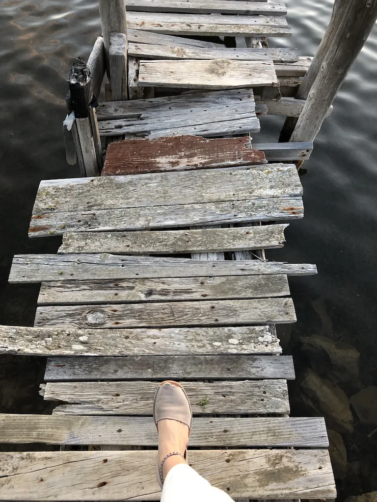 Feet stepping onto a weathered wooden jetty above the sea