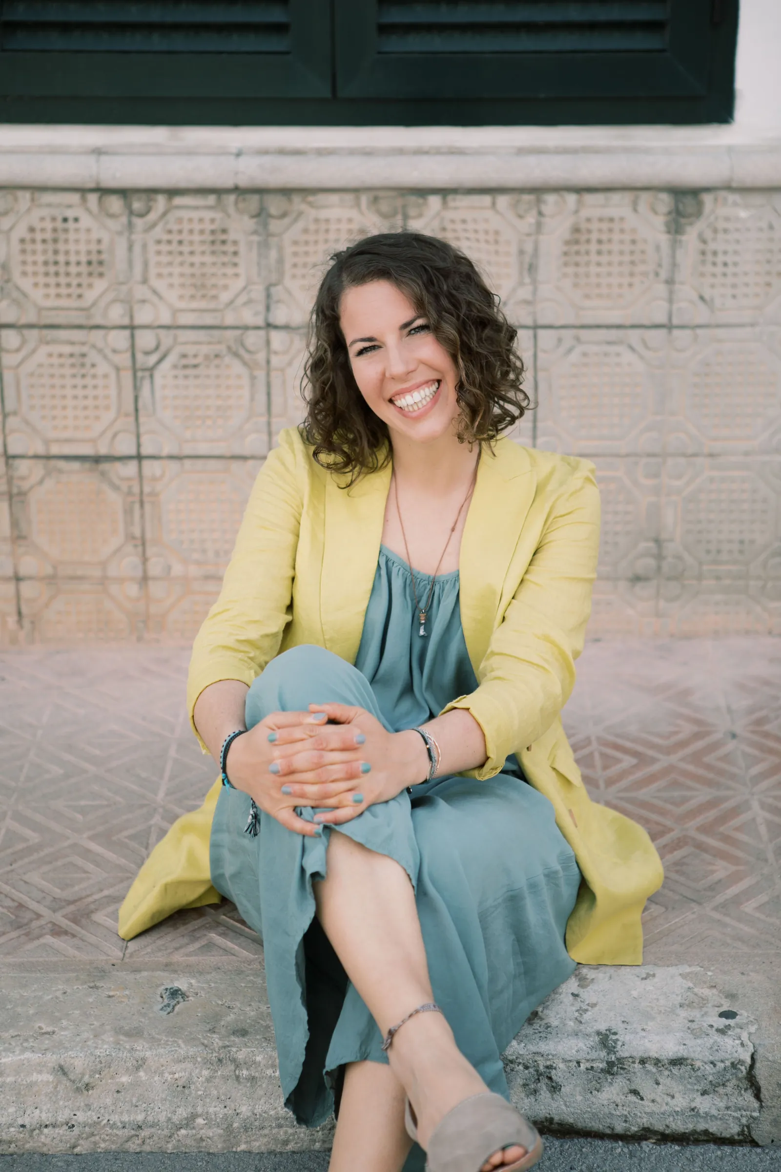Maria sitting on a stone step in a yellow blazer